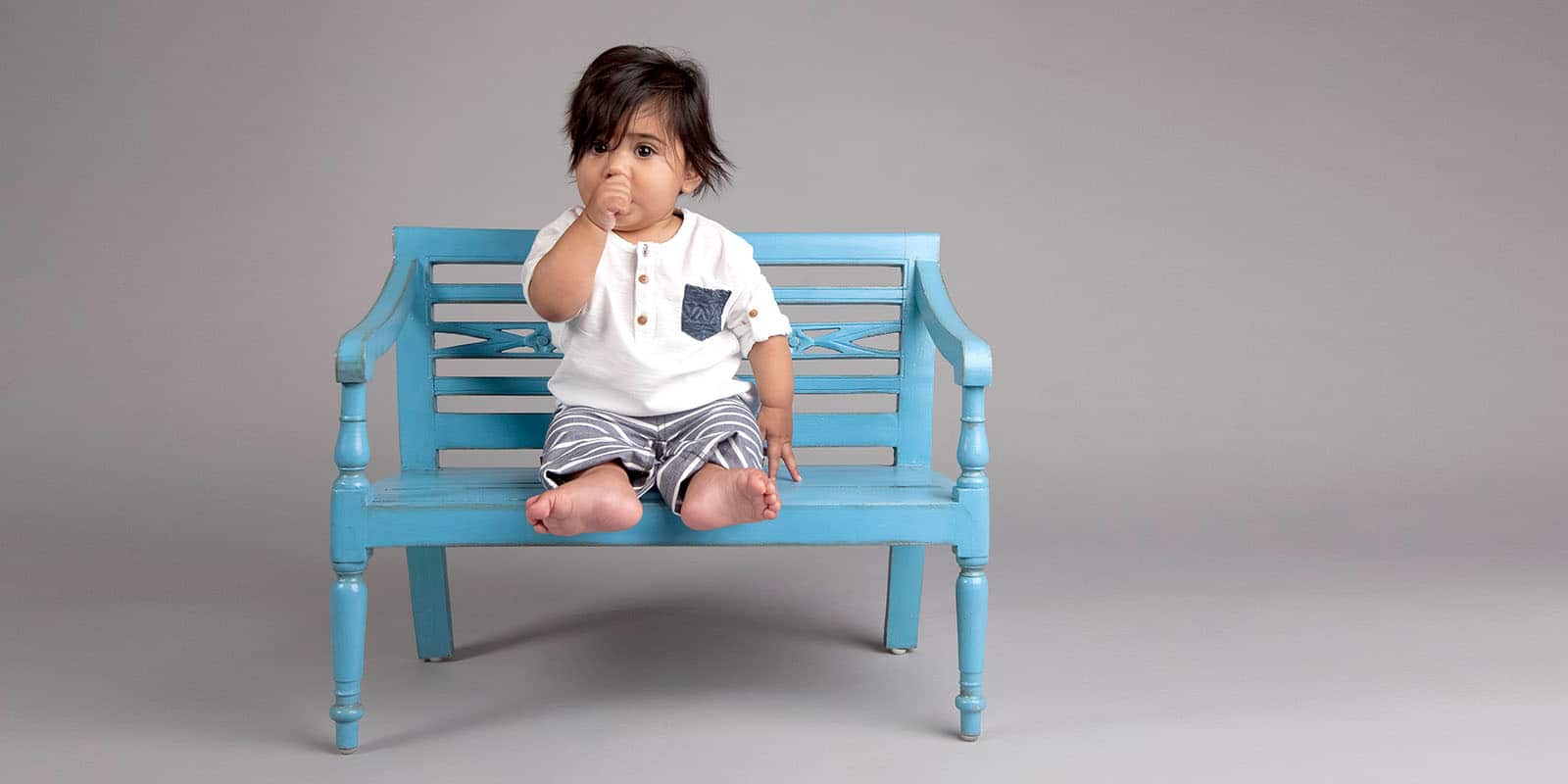 gorgeous baby boy hangs out on blue bench in private studio