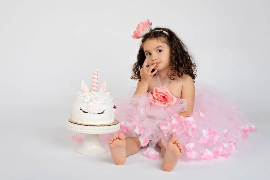 big sister posing with unicorn birthday cake