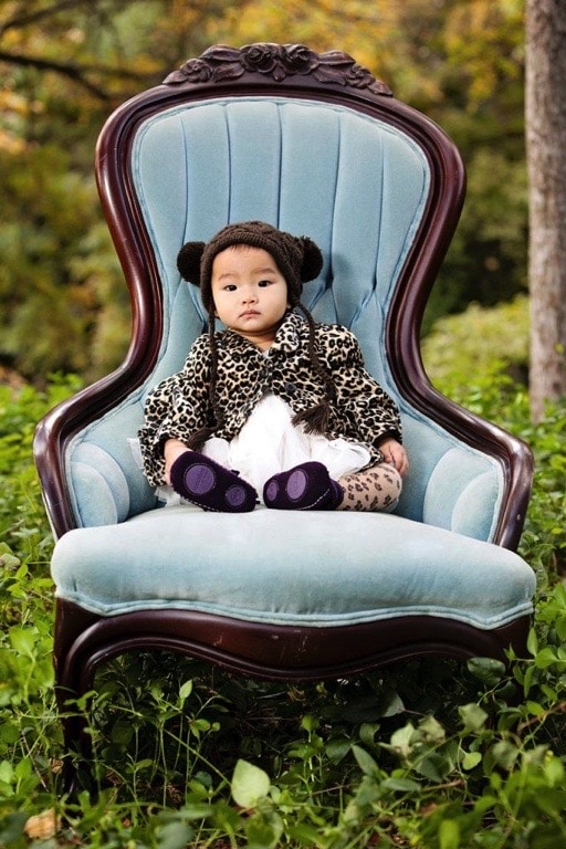 little girl poses in blue chair in a fun hat and jacket