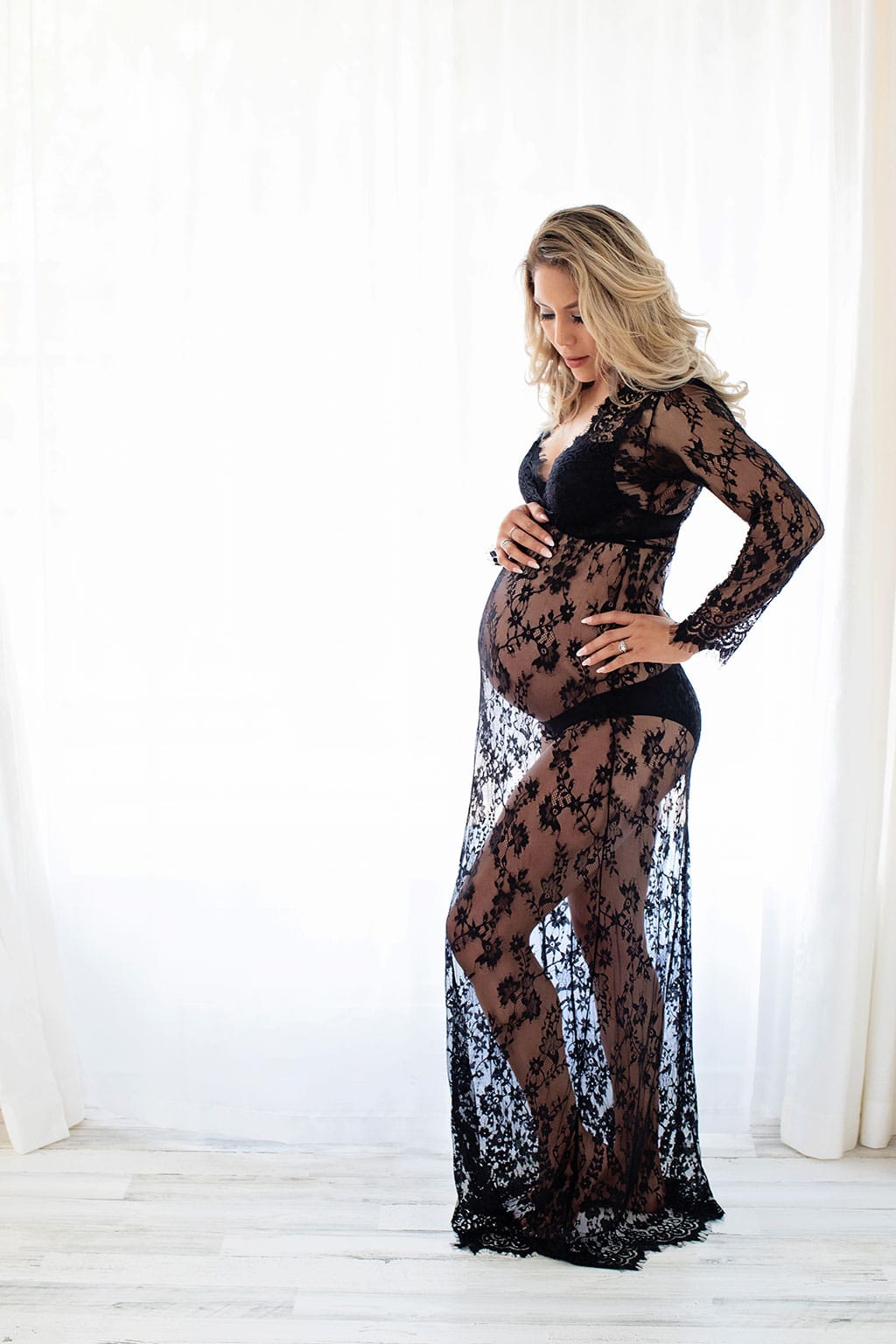 expecting mom poses in floor-length lace dress showing off her belly