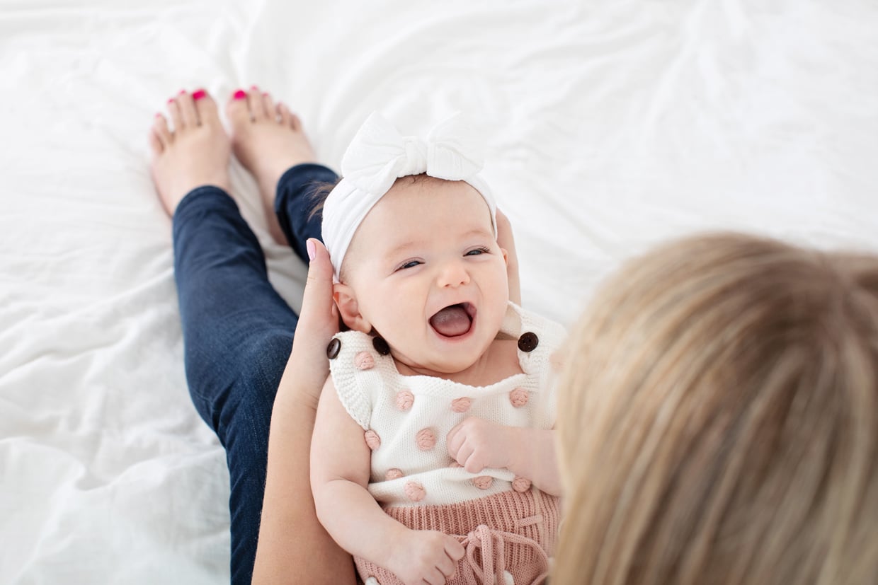 happiest two-month-old baby girl smiling in her moms lap