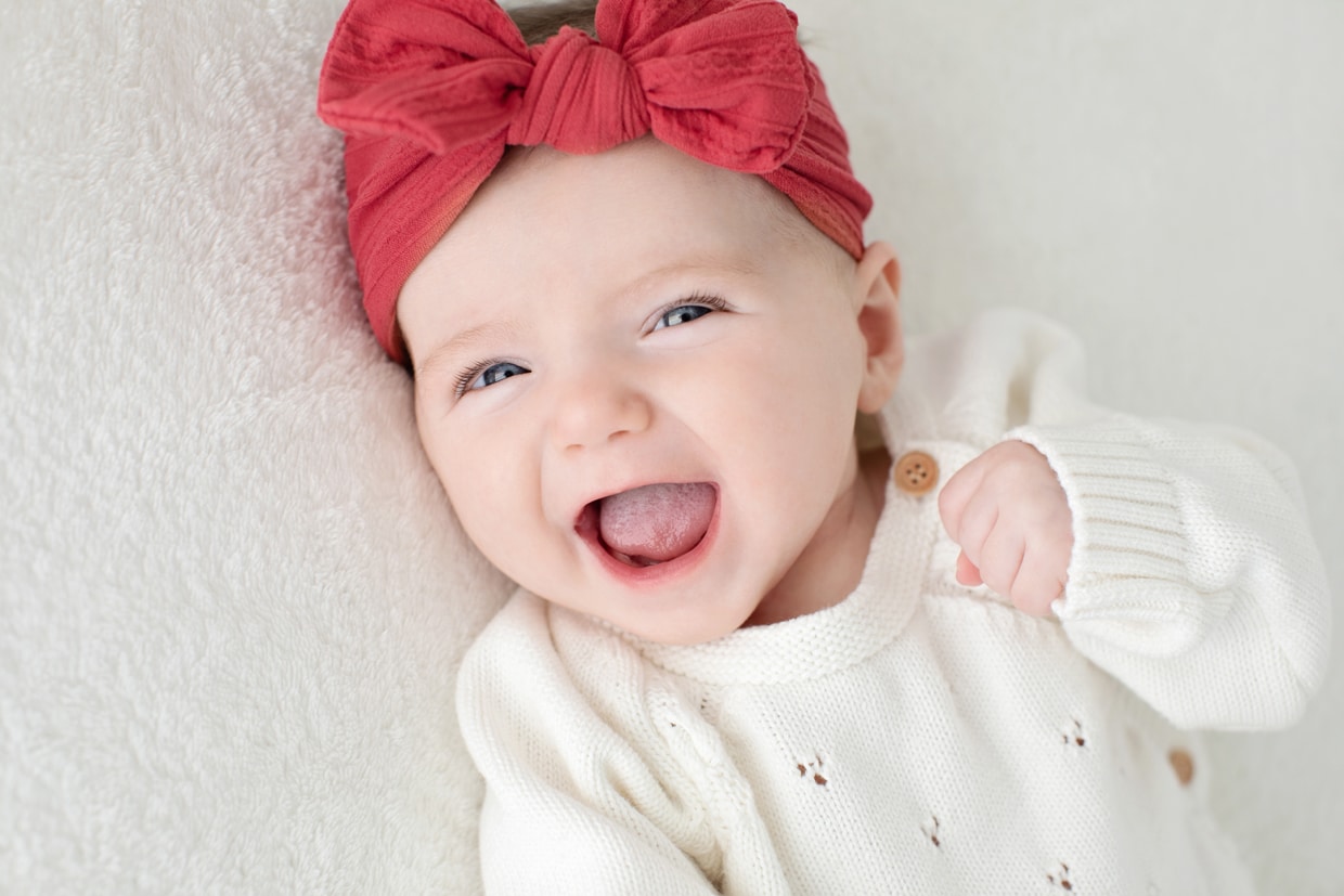 happiest newborn baby girl smiling big at the camera with red bow on her head