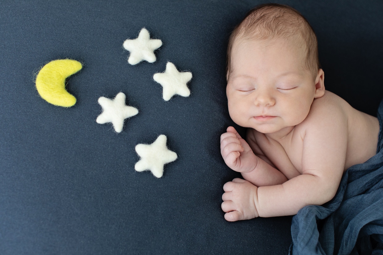newborn baby snuggled up on blue backdrop with stars and a moon