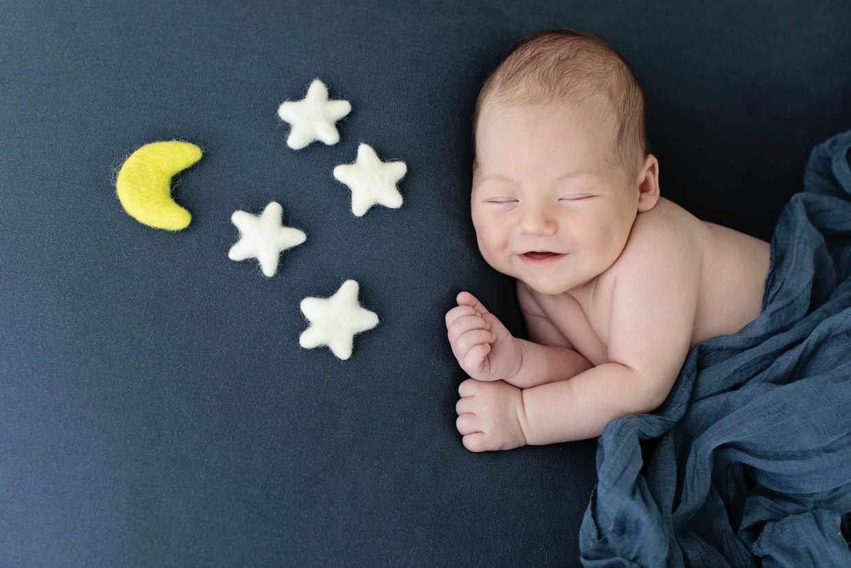 newborn baby snuggled up on blue backdrop with stars and a moon