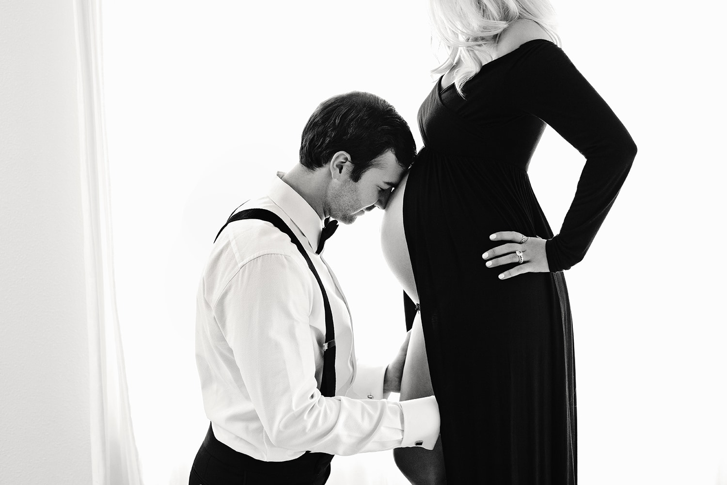 A husband leans his head on his wife's pregnant belly.