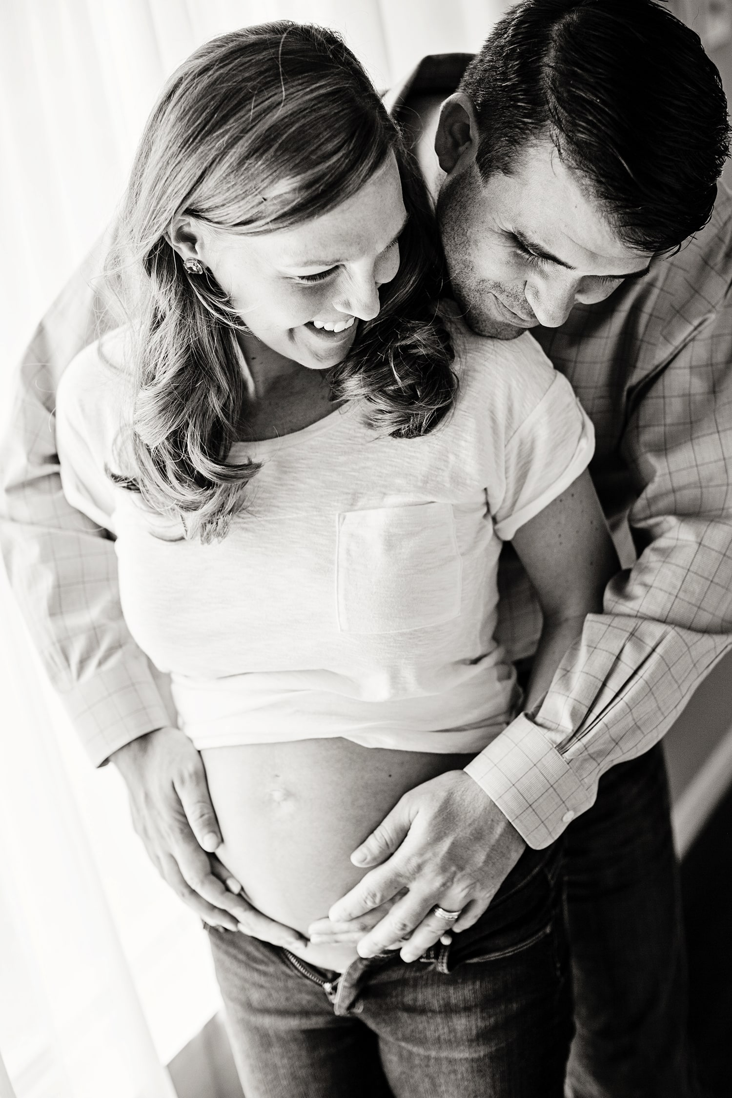 A husband and wife smile while he touches her belly.