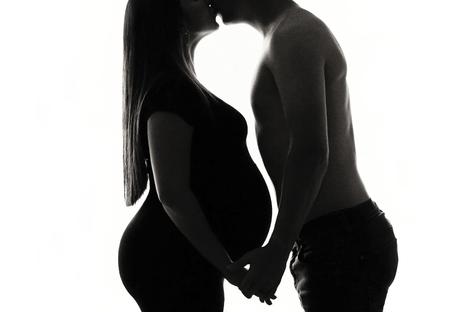 A husband and wife kiss over the wife's belly.