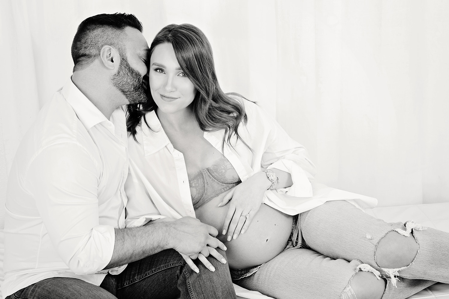 A husband kisses his wife's cheek while she smiles at the camera.