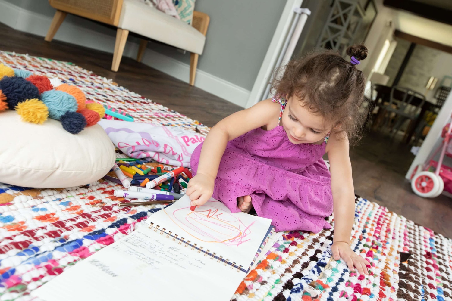 A little girl colors on a colorful rug.