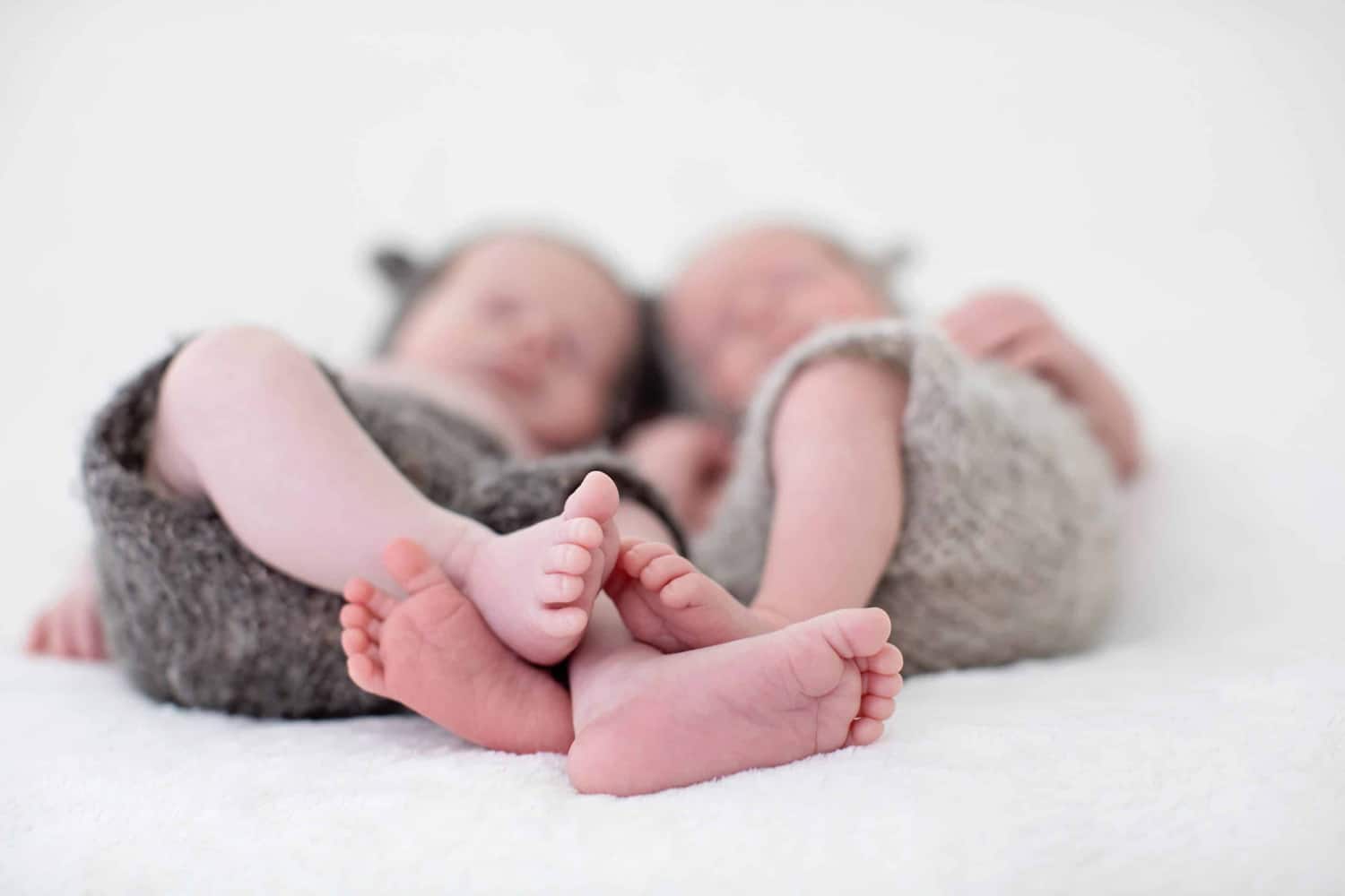 Two newborn babies lay with their feet intertwined.