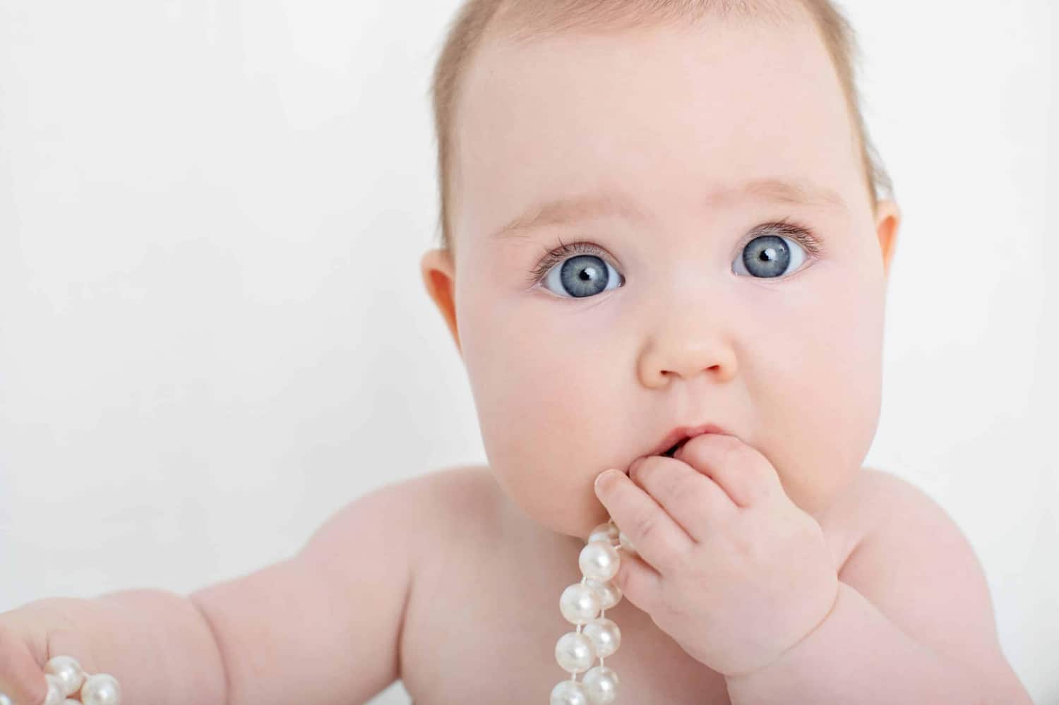 A baby chews on a plastic string of pearls.