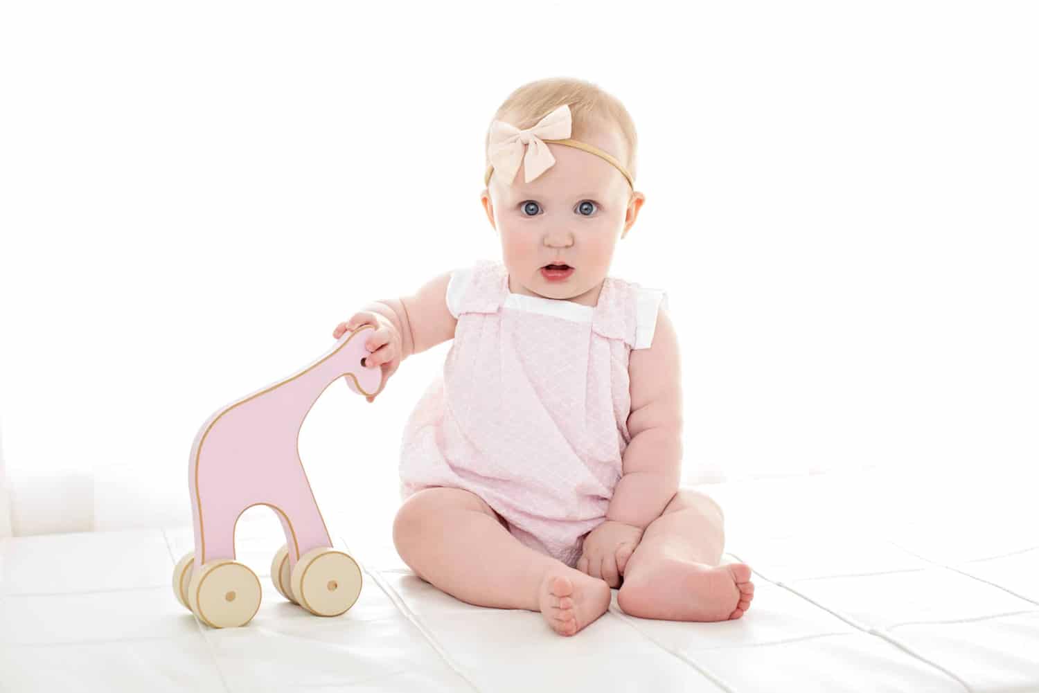 A baby girl plays with a pink wooden elephant.