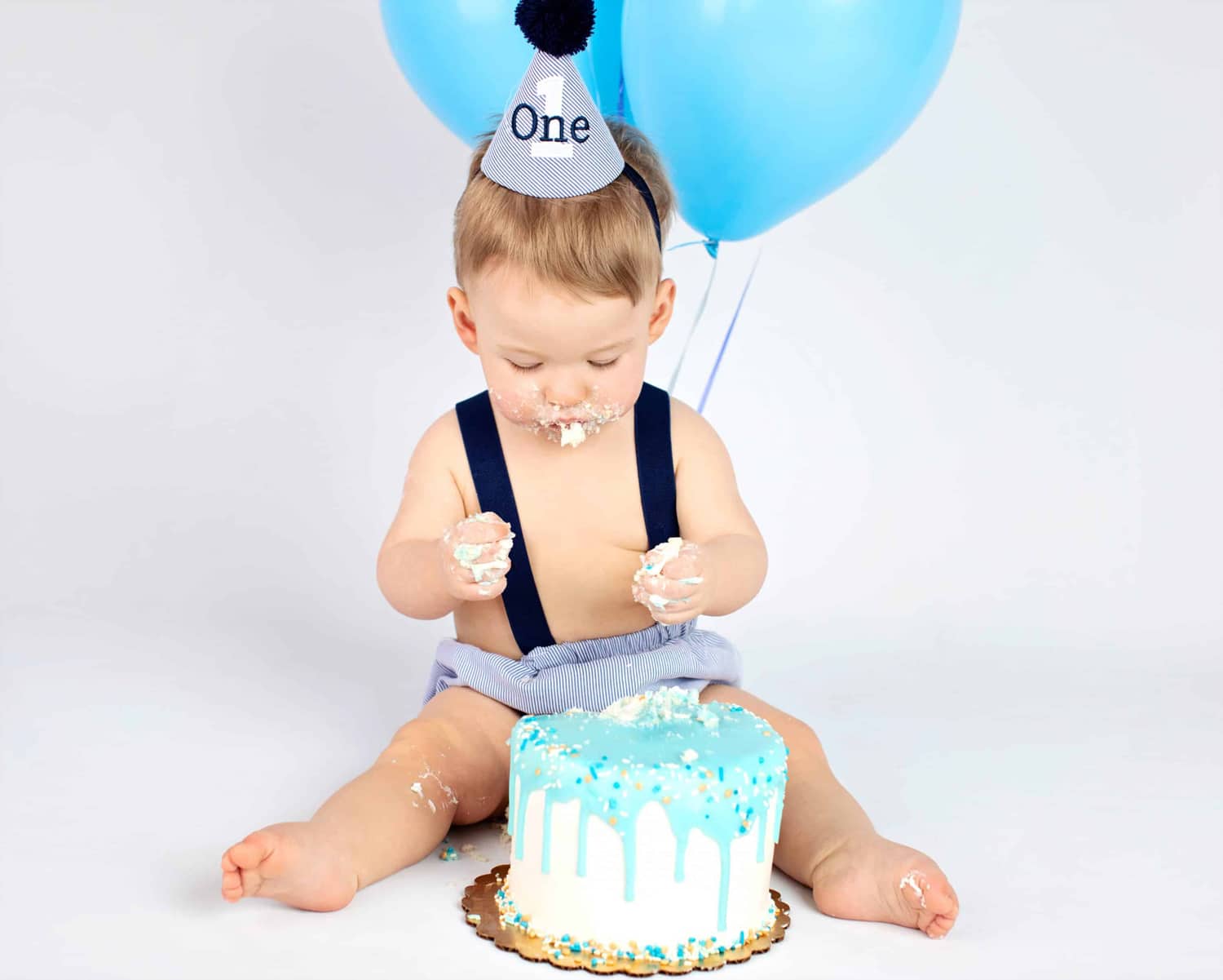 A one year old baby eats a blue birthday cake.