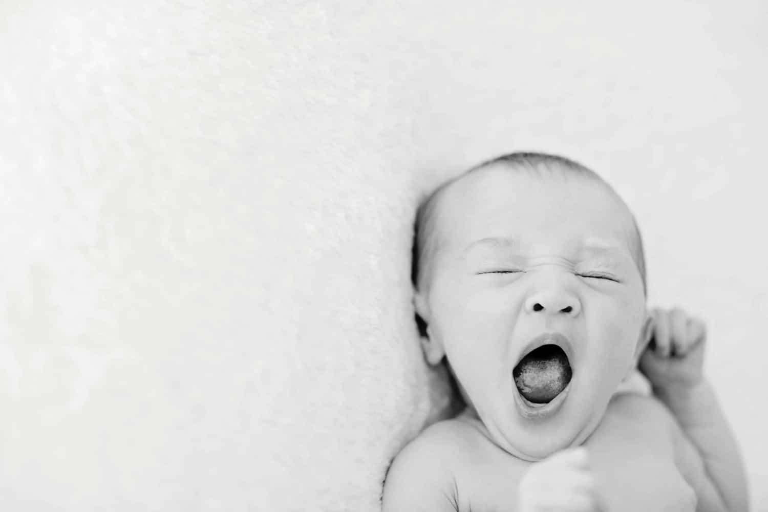A baby yawns on a white pillow.