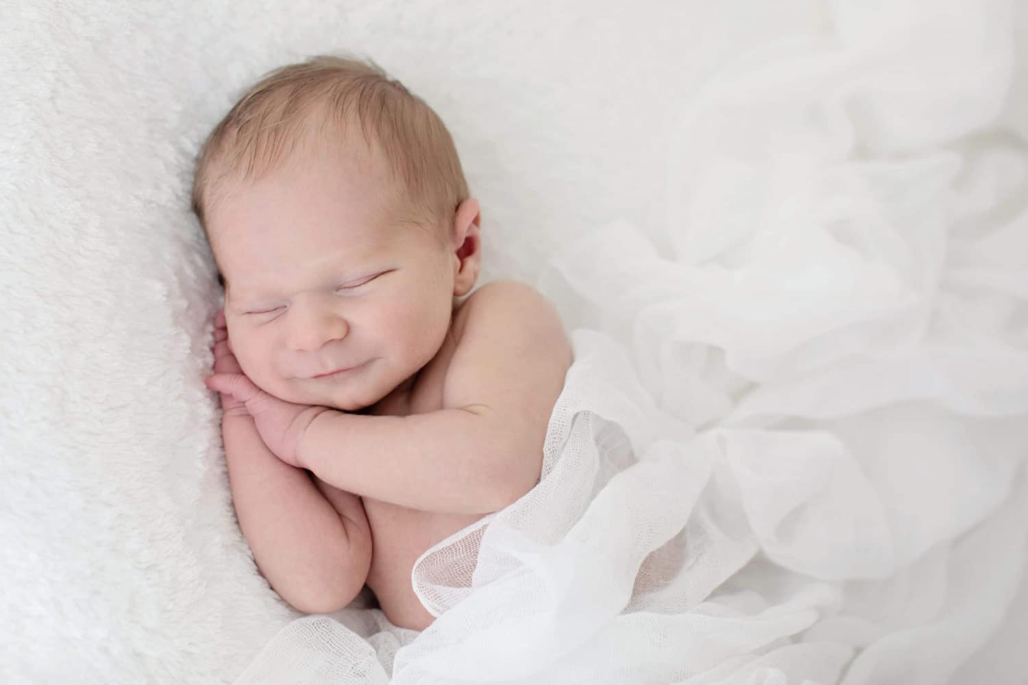 A baby snuggles on a white pillow.