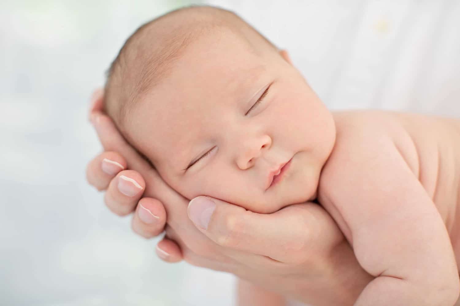 A baby's head lays in someone's hand.
