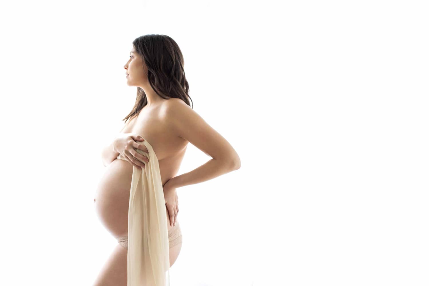 A boudoir maternity photo with a white sheet.