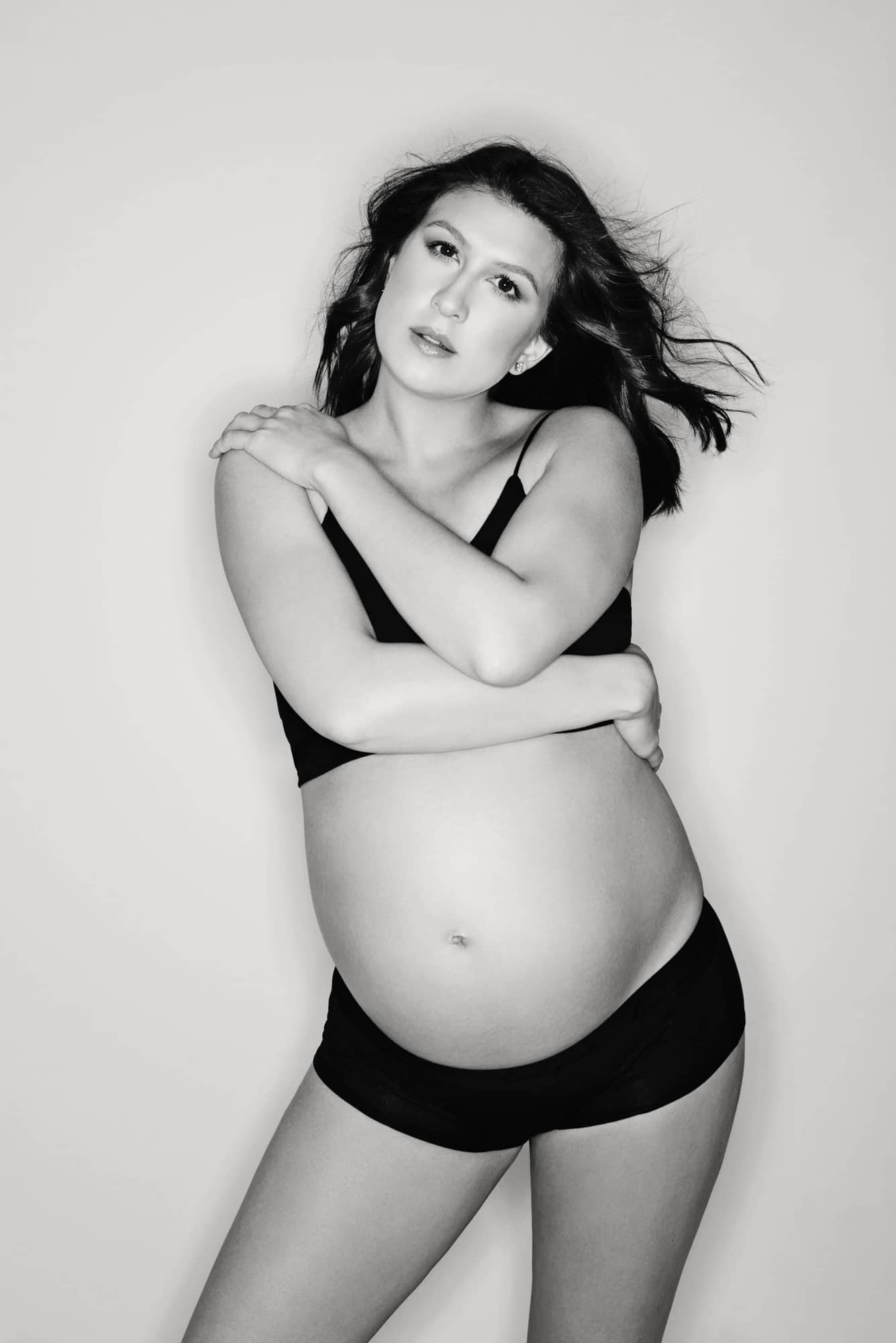 A boudoir maternity photo of a woman in black underwear.