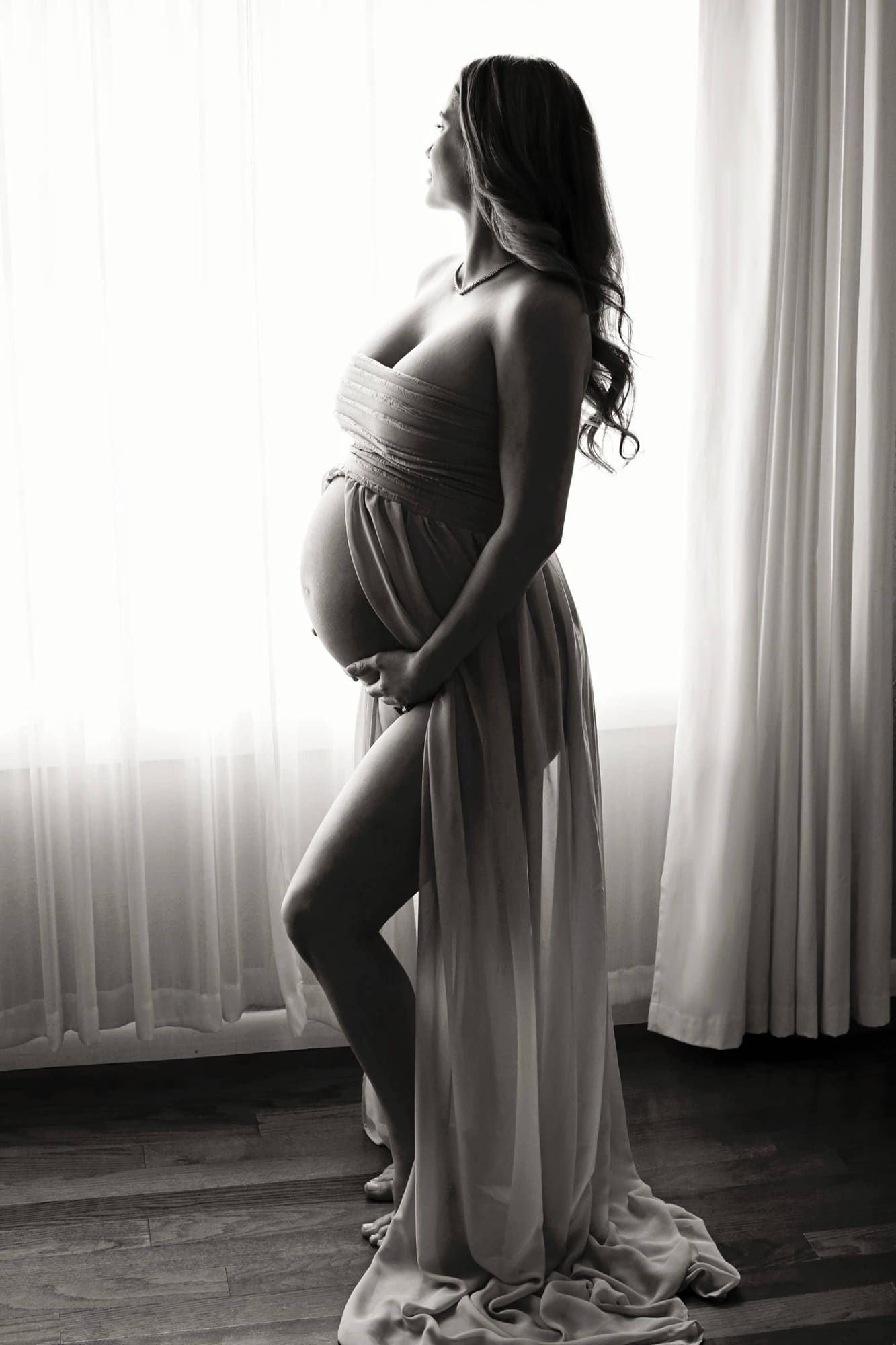 A boudoir maternity portrait in front of a window.