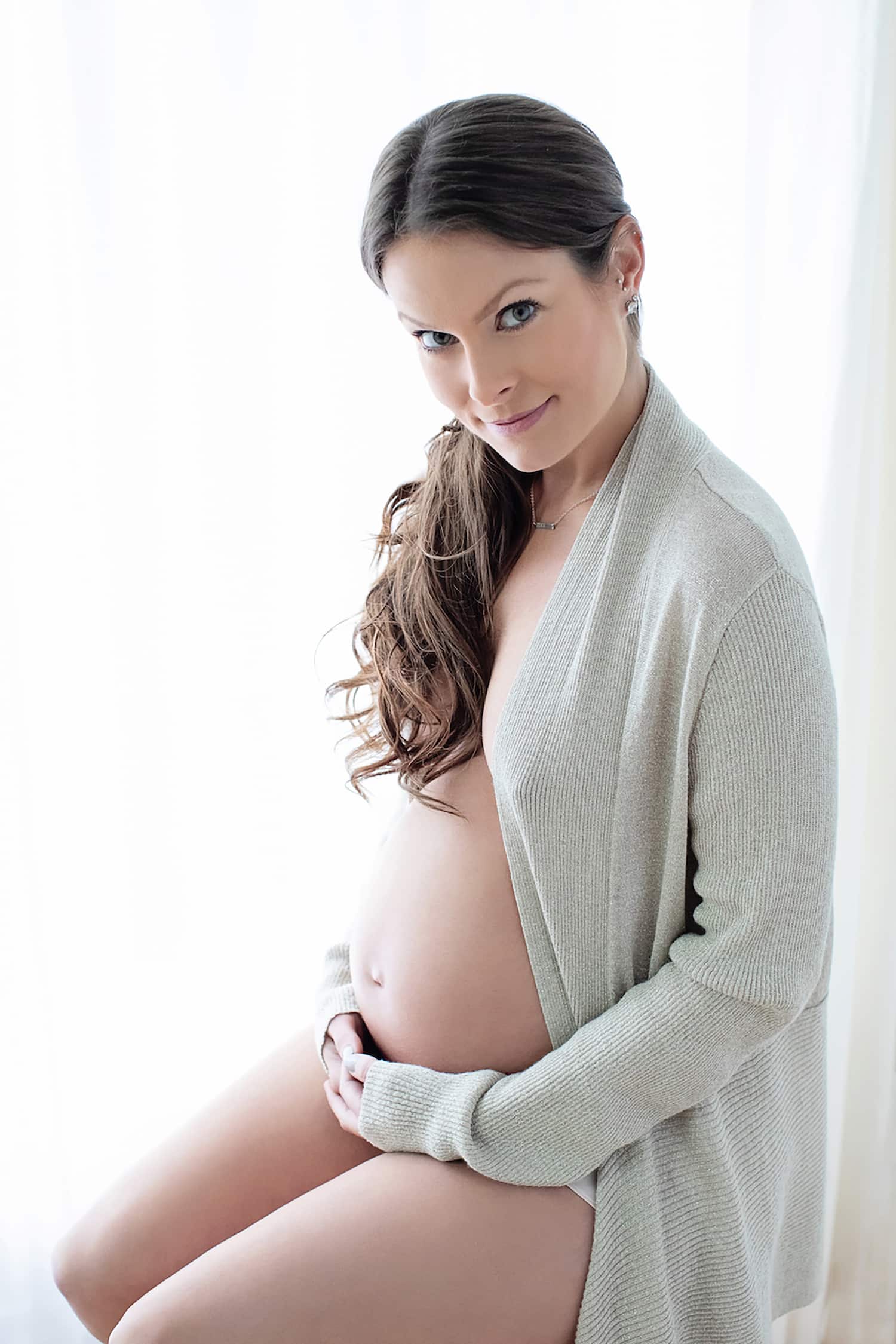A woman with a messy ponytail in a maternity shoot.