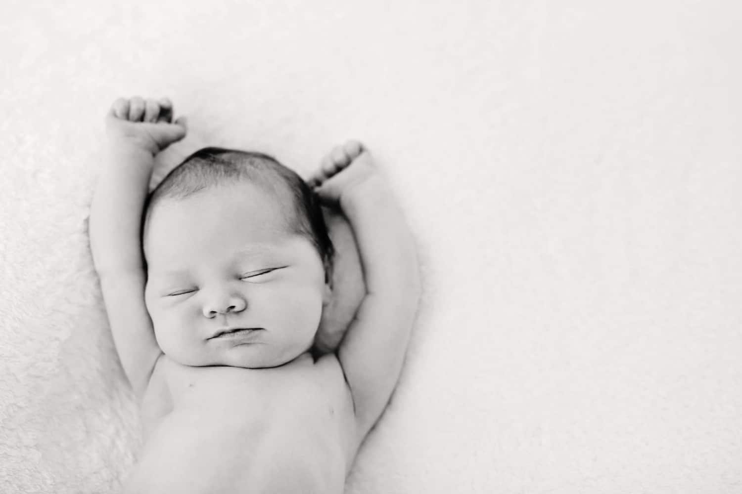 A newborn baby stretches on a soft background.