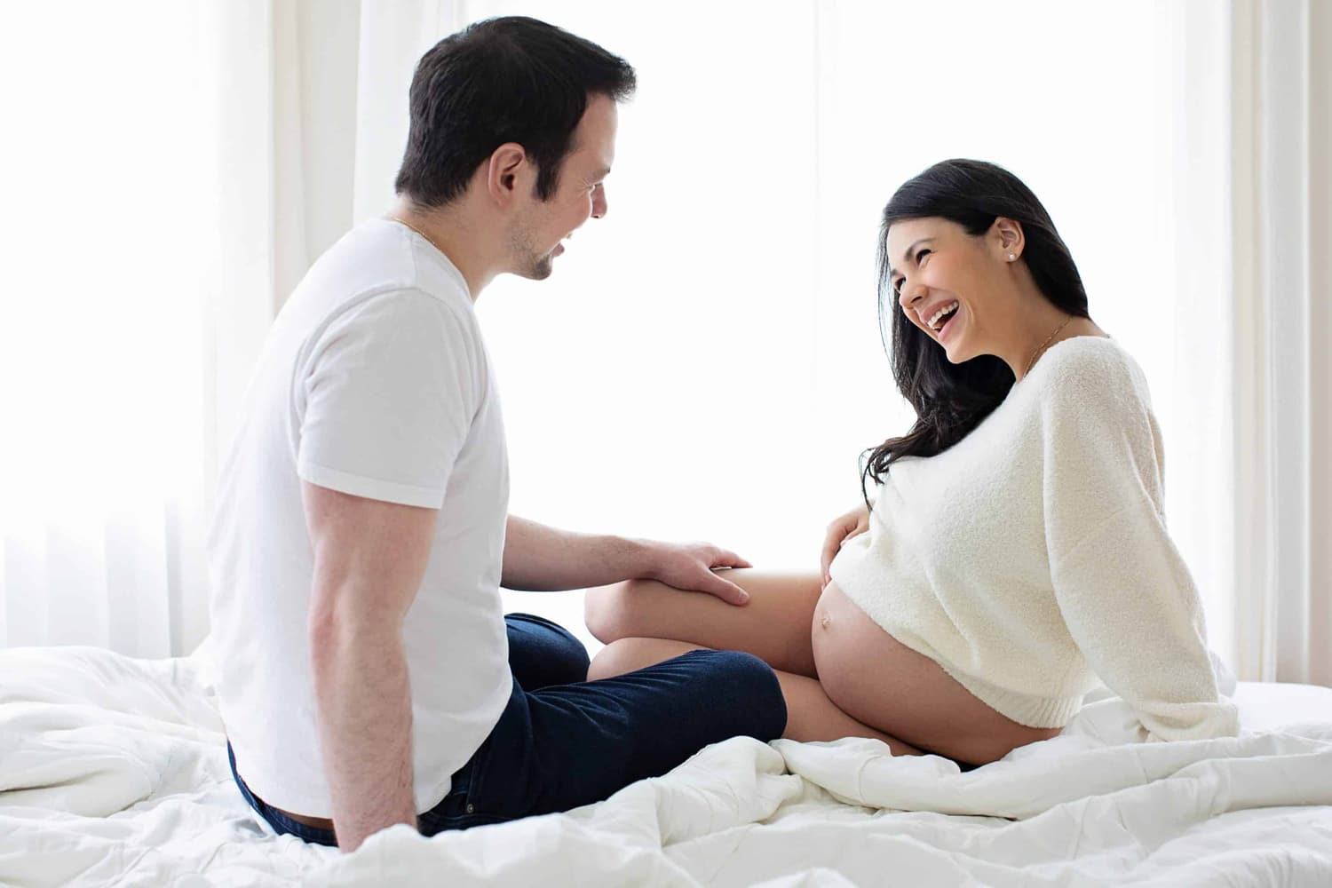 A couple smiles at each other during a maternity shoot.