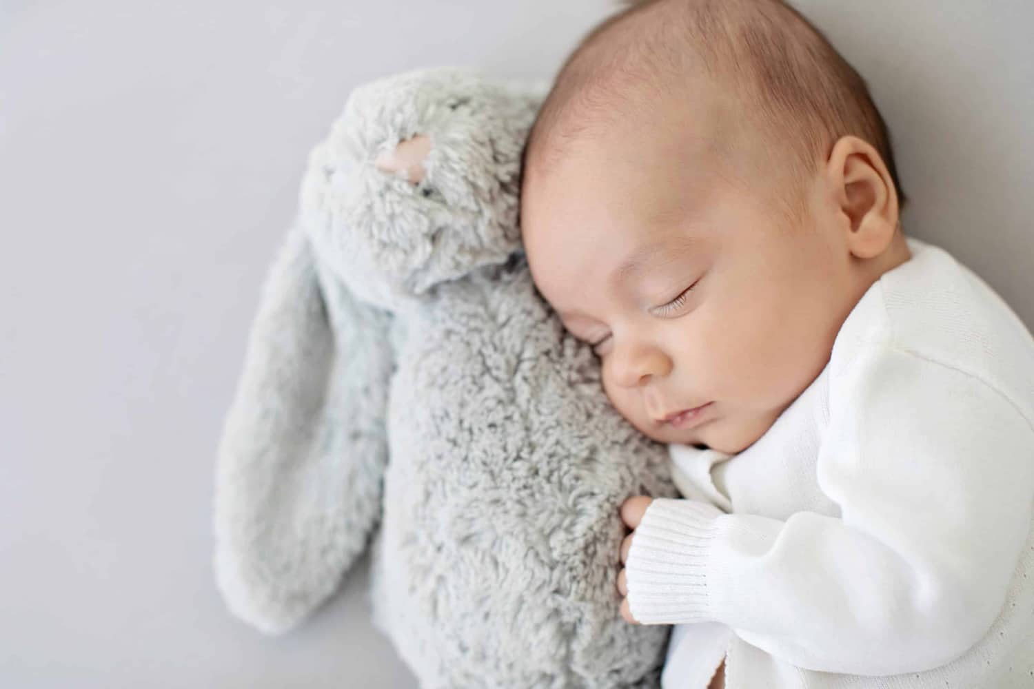 A baby snuggles with a stuffed rabbit.