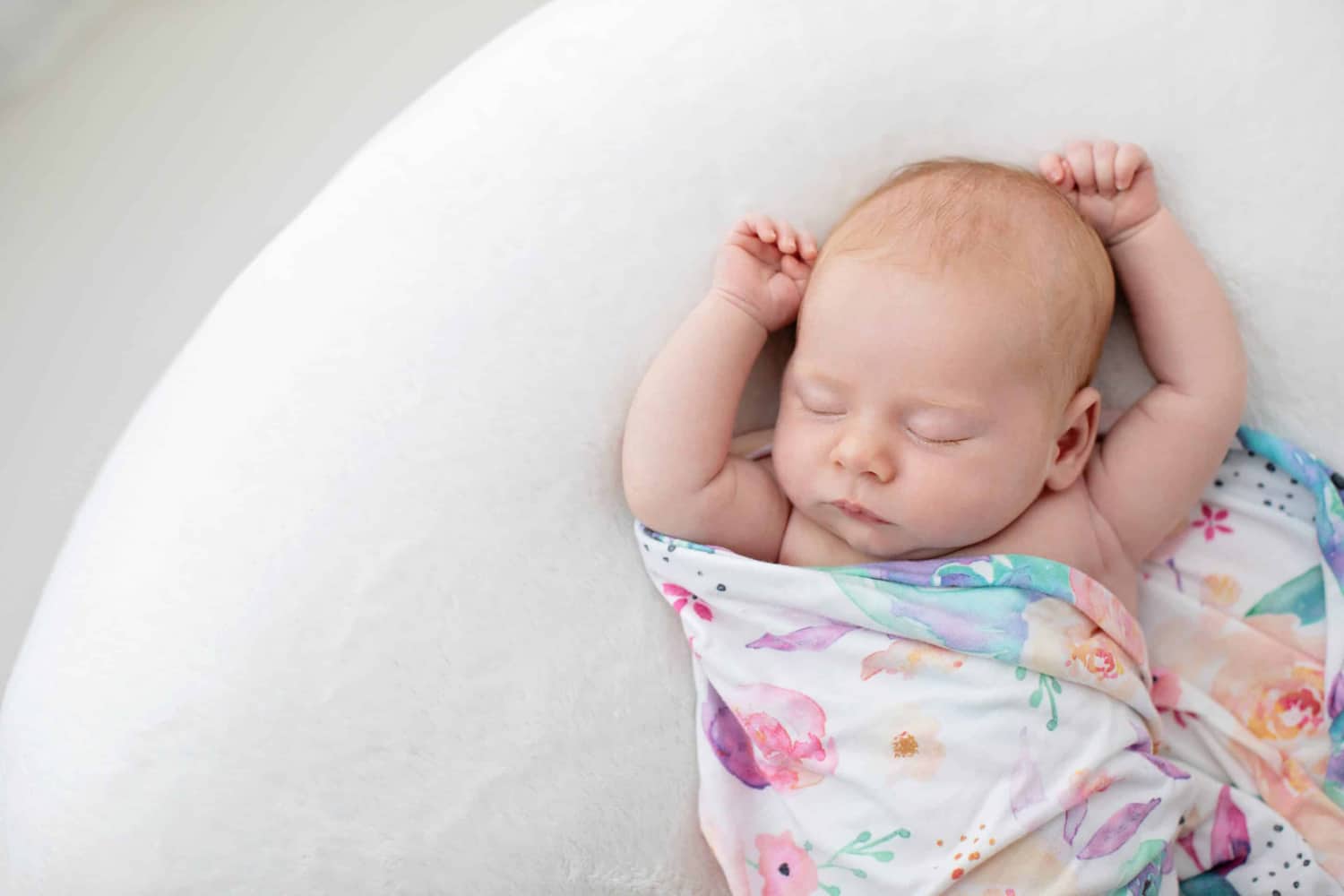 A baby stretches in a colorful blanket.