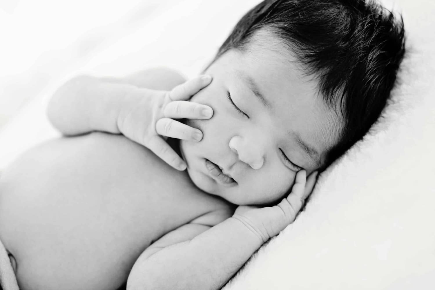 A baby touches its cheeks in a newborn photo.