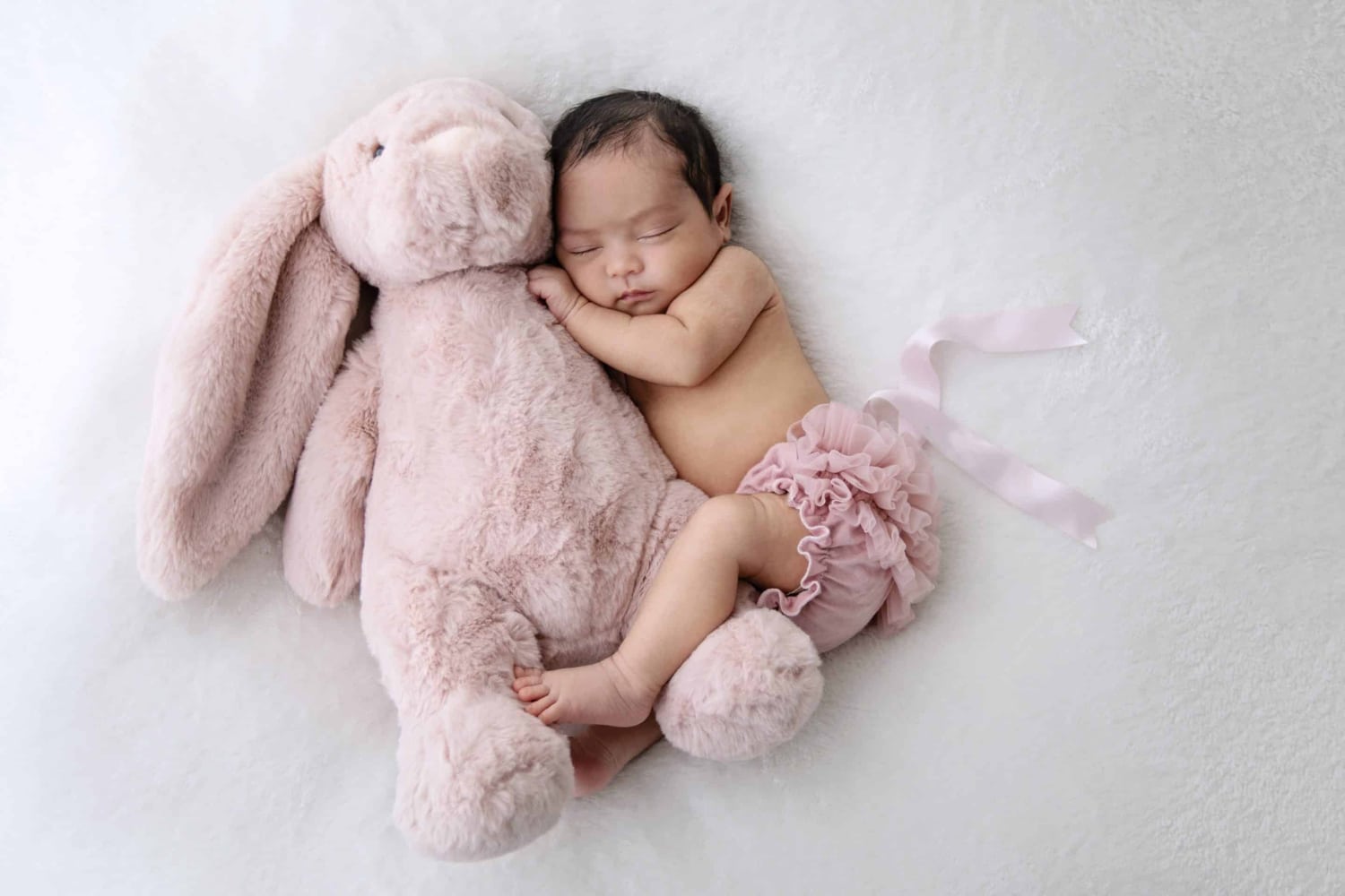 A newborn baby snuggles with a stuffed rabbit.