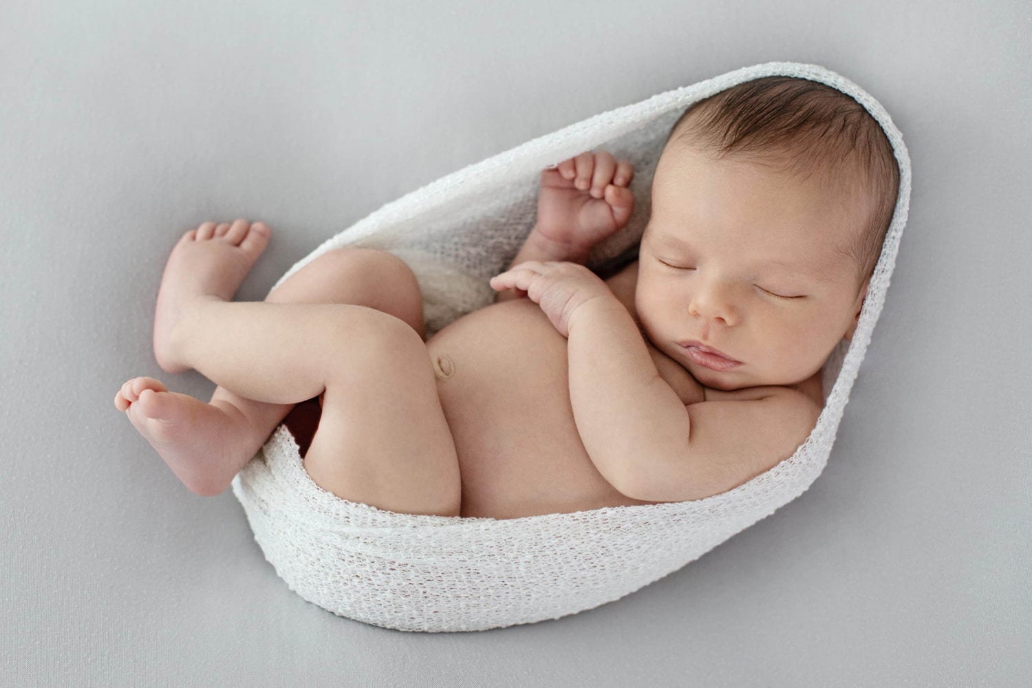 A newborn baby wrapped in a white swaddle.