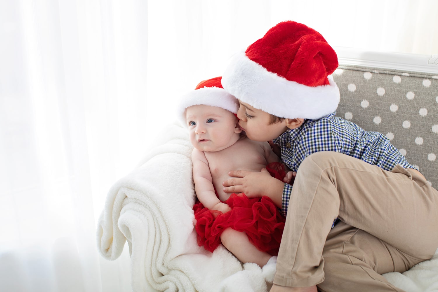 A boy in a Santa hat kisses his baby sibling.