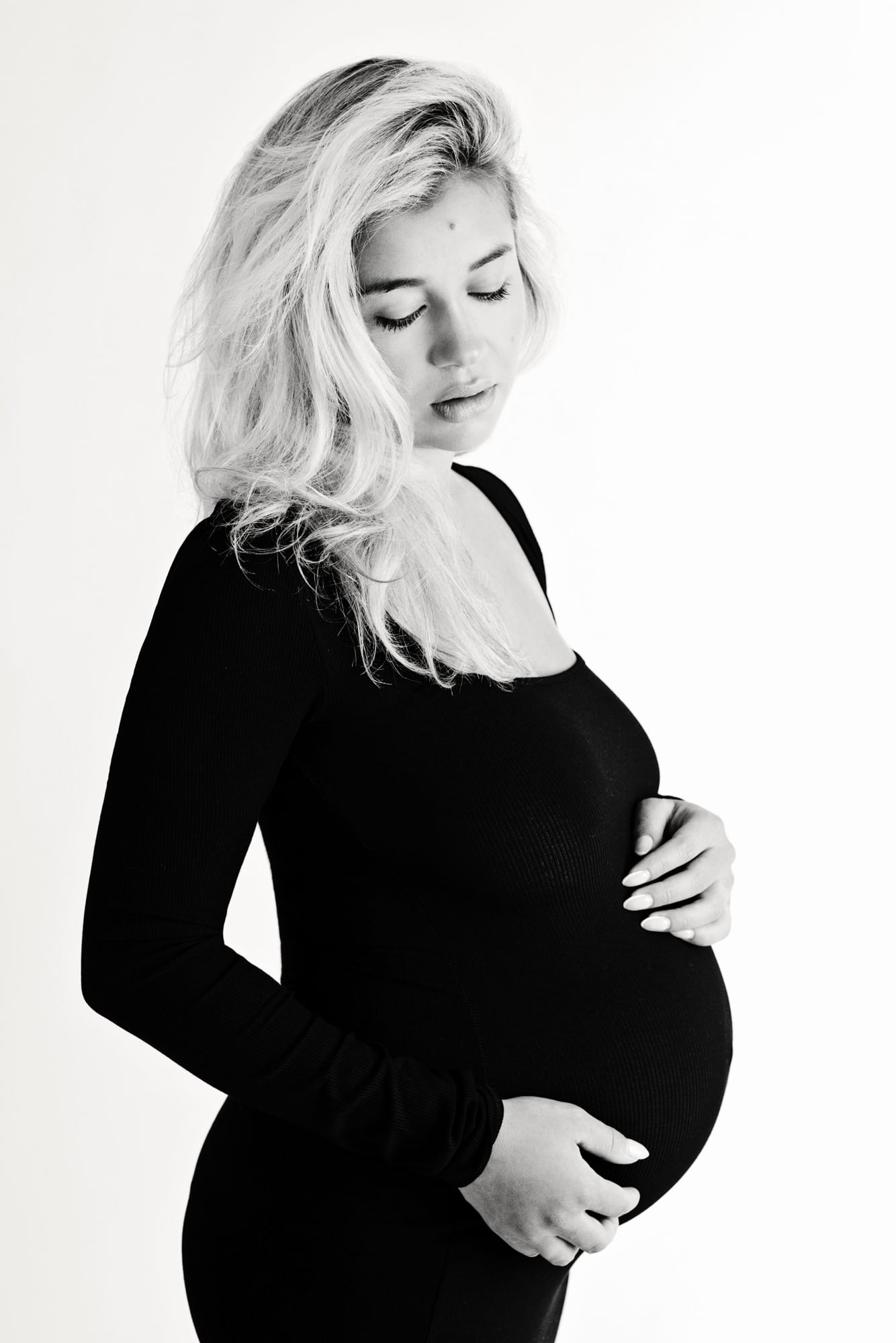 A pregnant woman in a black dress holds her belly.