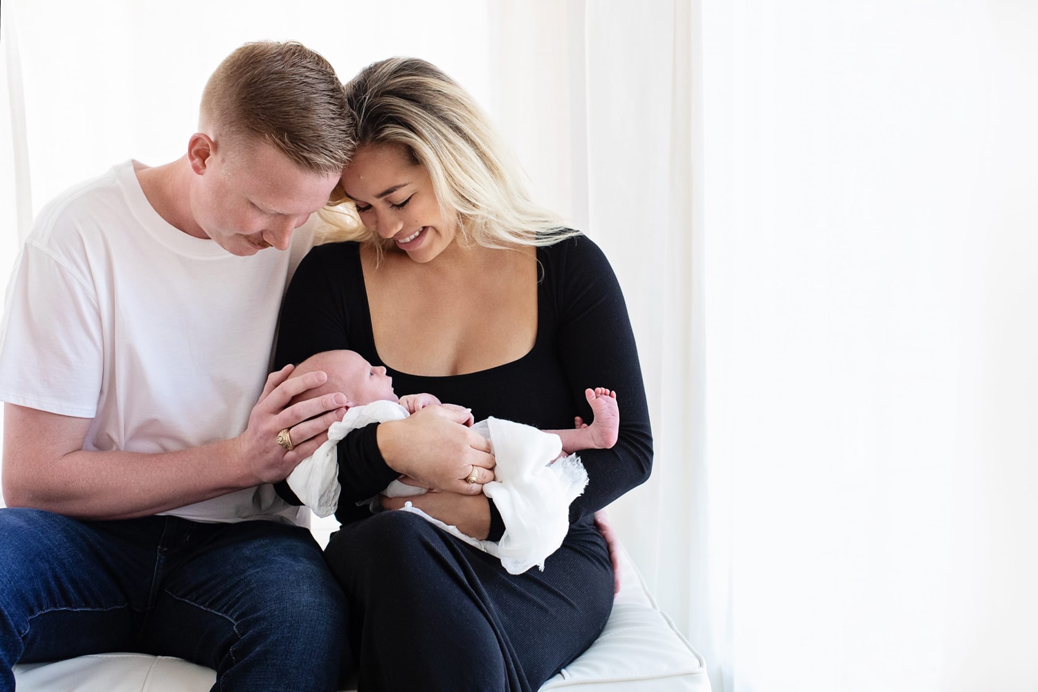 A woman and her husband smile at their newborn baby.