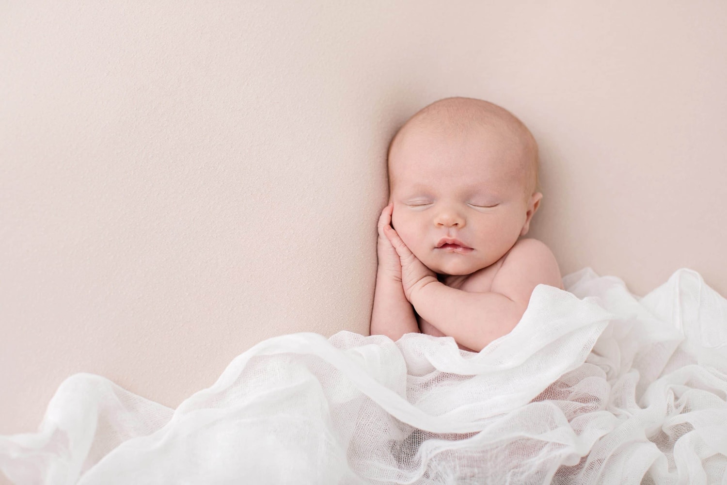 A newborn baby sleeps on a white background.