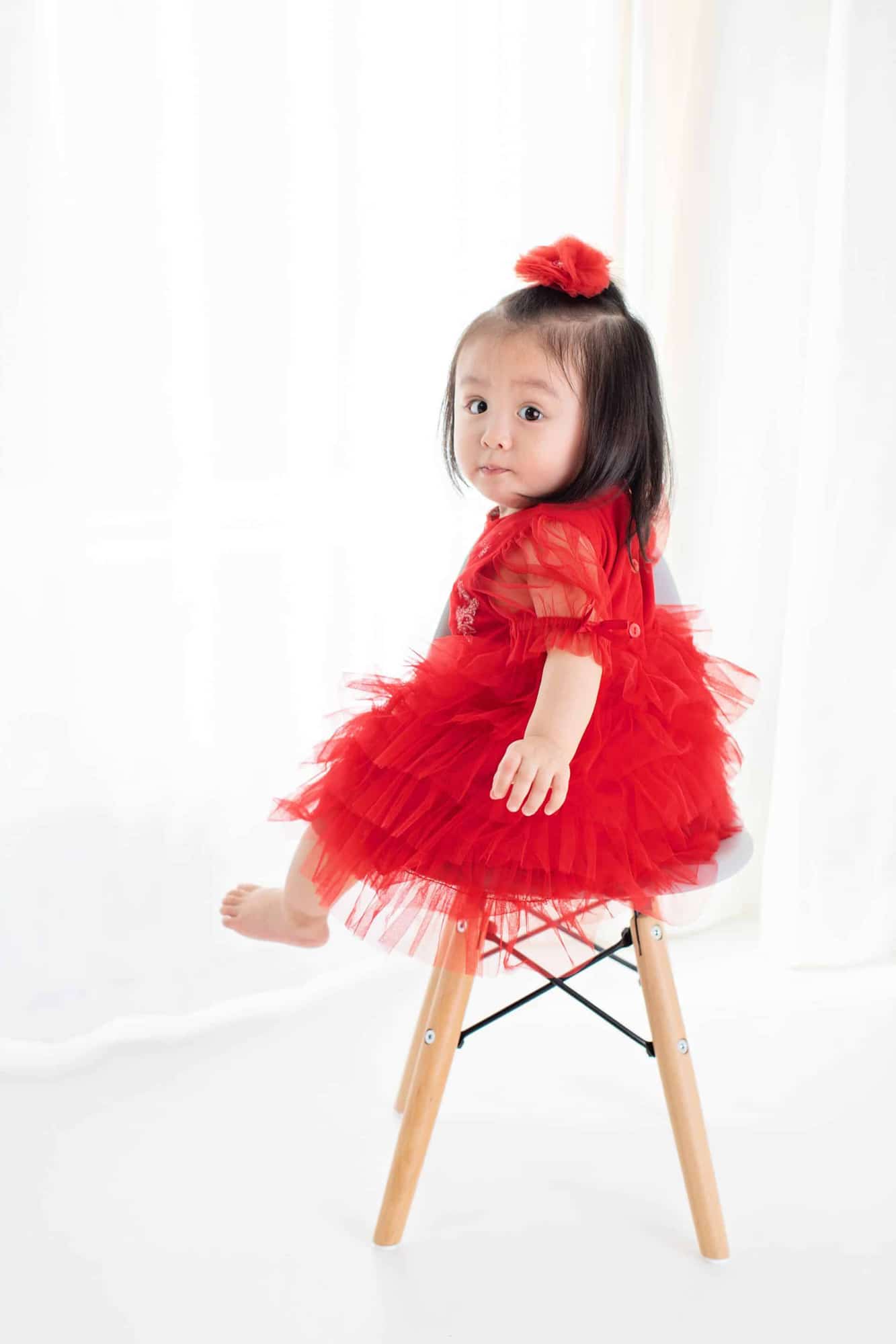 A girl in a bright red dress sits on a stool.