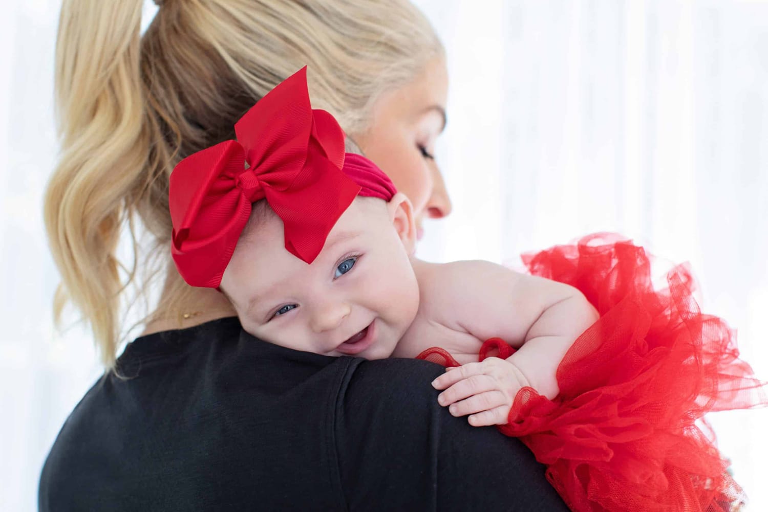 A mom holds her baby wearing a big red bow.