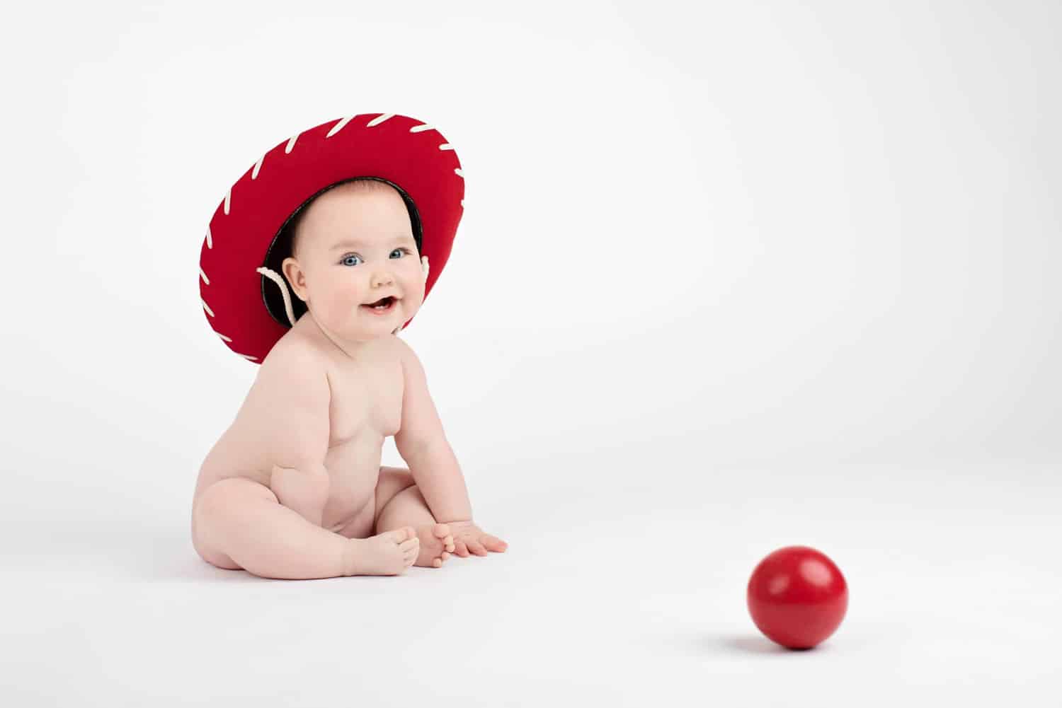 A baby in a red hat plays with a red ball.