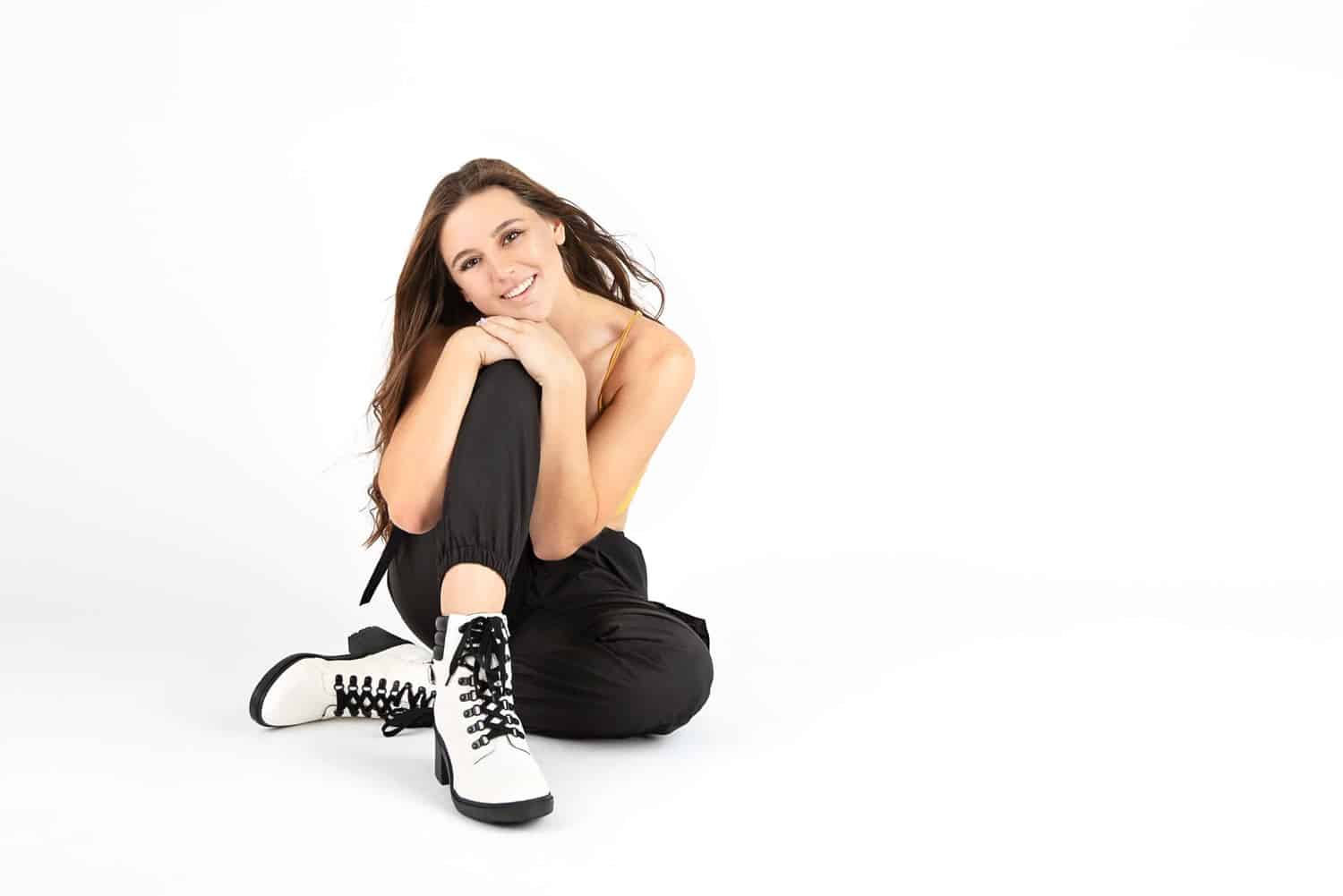 A girl takes senior photos in white boots and black pants.