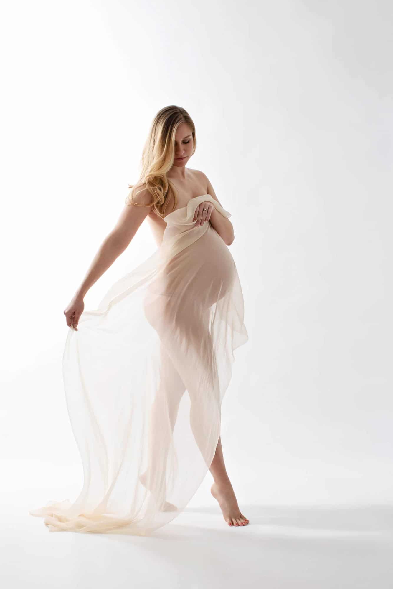A pregnant woman walks in a white gauzy gown.
