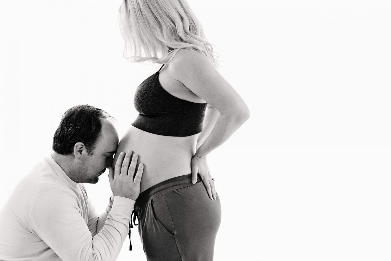 A man presses his head to his wife's belly in a maternity portrait.
