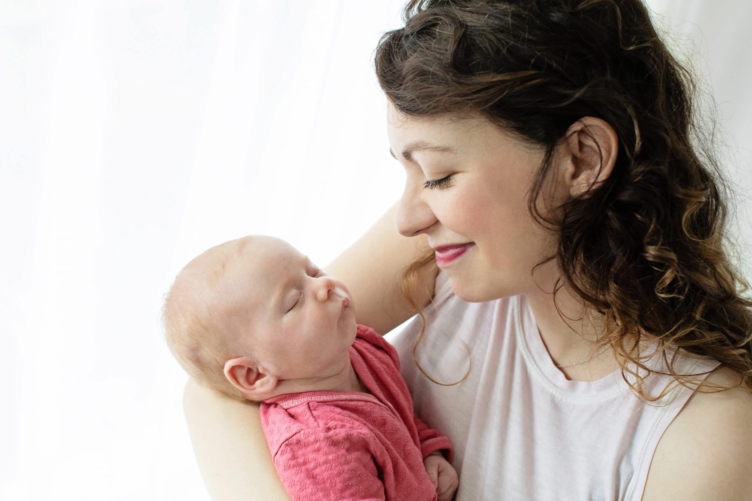 A mom smiles at her newborn wearing a pink onesie.