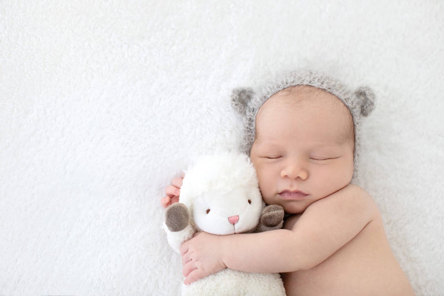 Newborn baby cuddles with stuffed sheep.