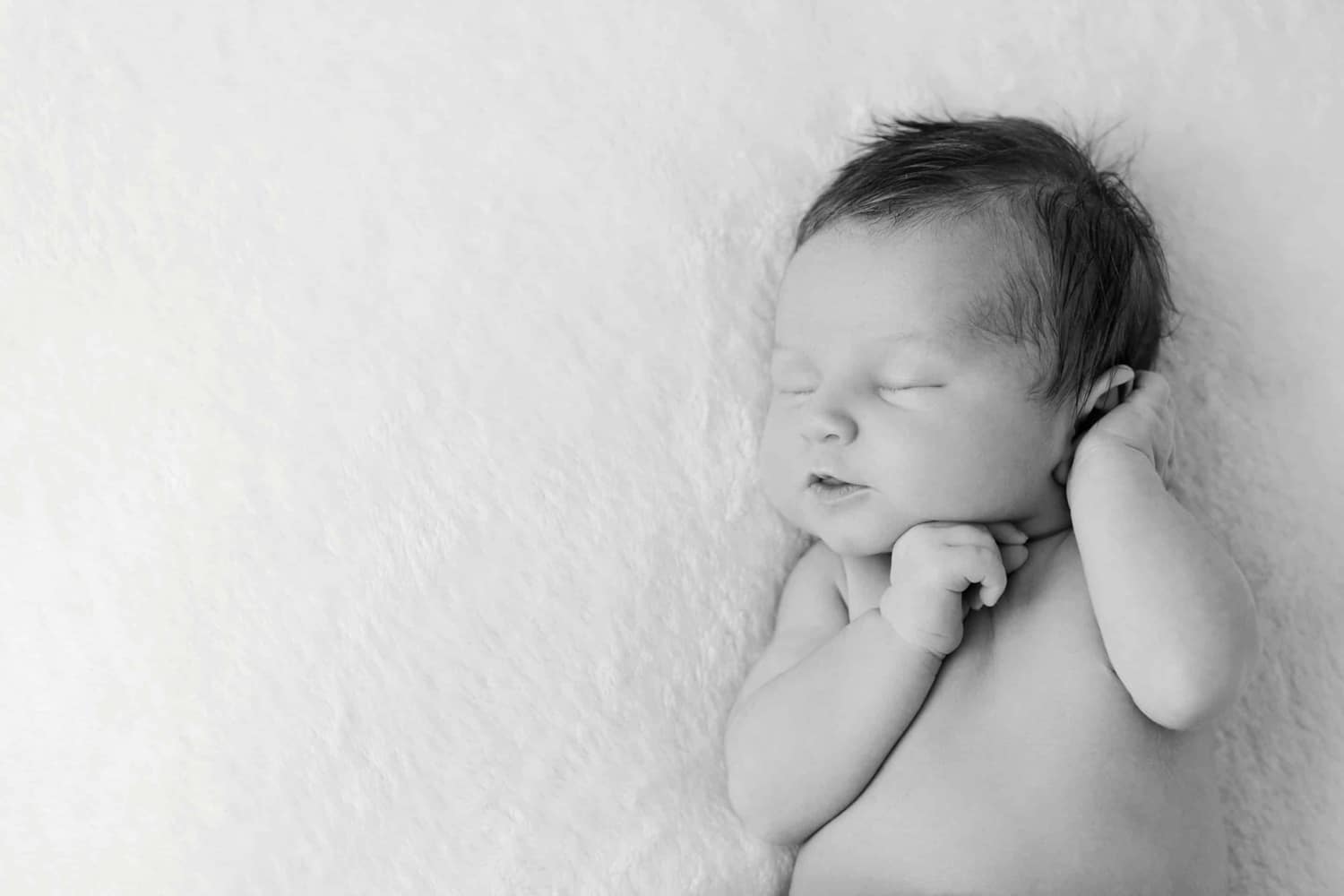 A newborn baby lies on a white fuzzy blanket.