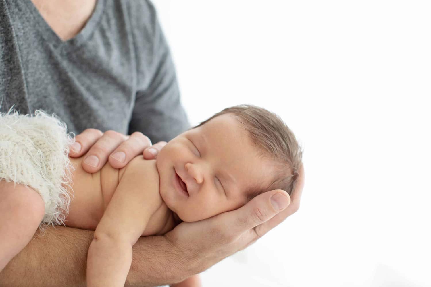 A newborn baby smiles in its dad's arm.