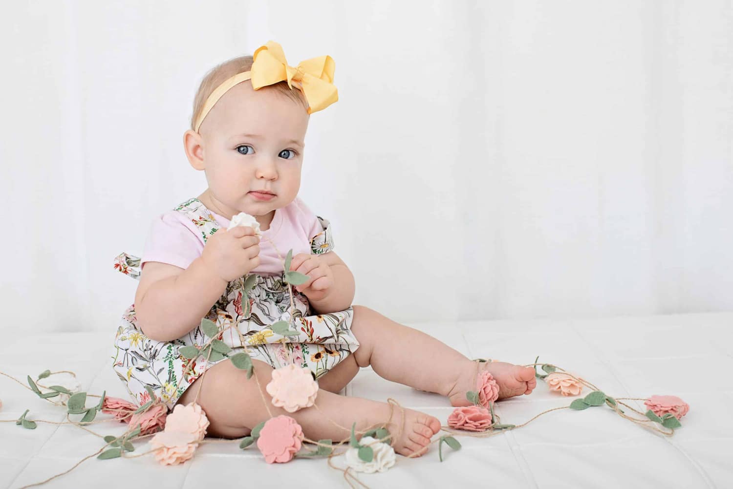Baby in floral dress holding garland.