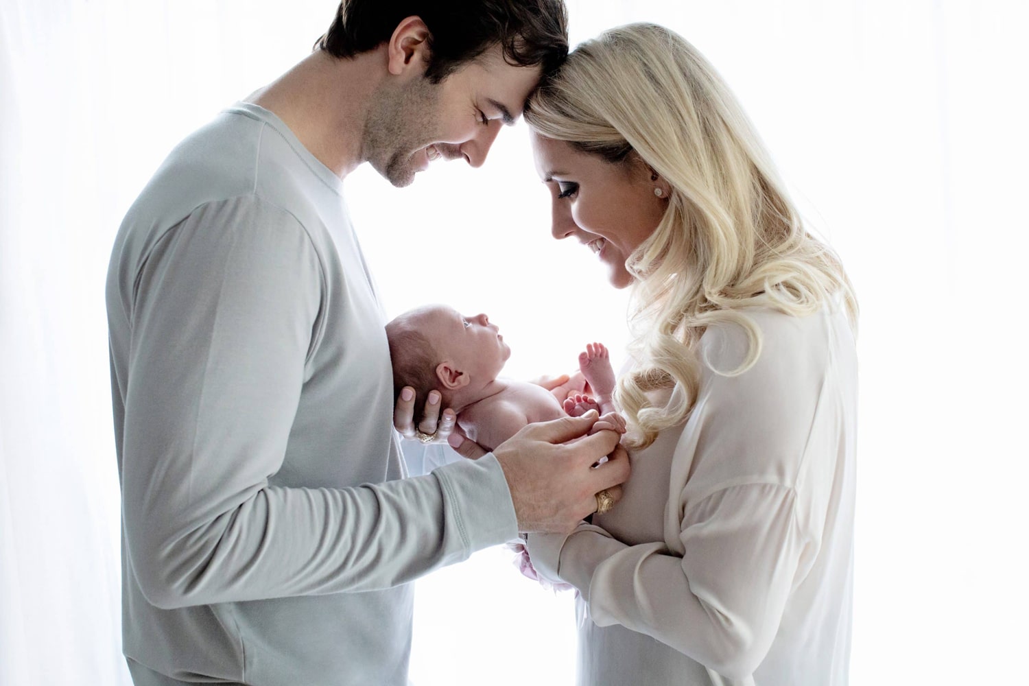 A couple looks down and smiles at their new baby.