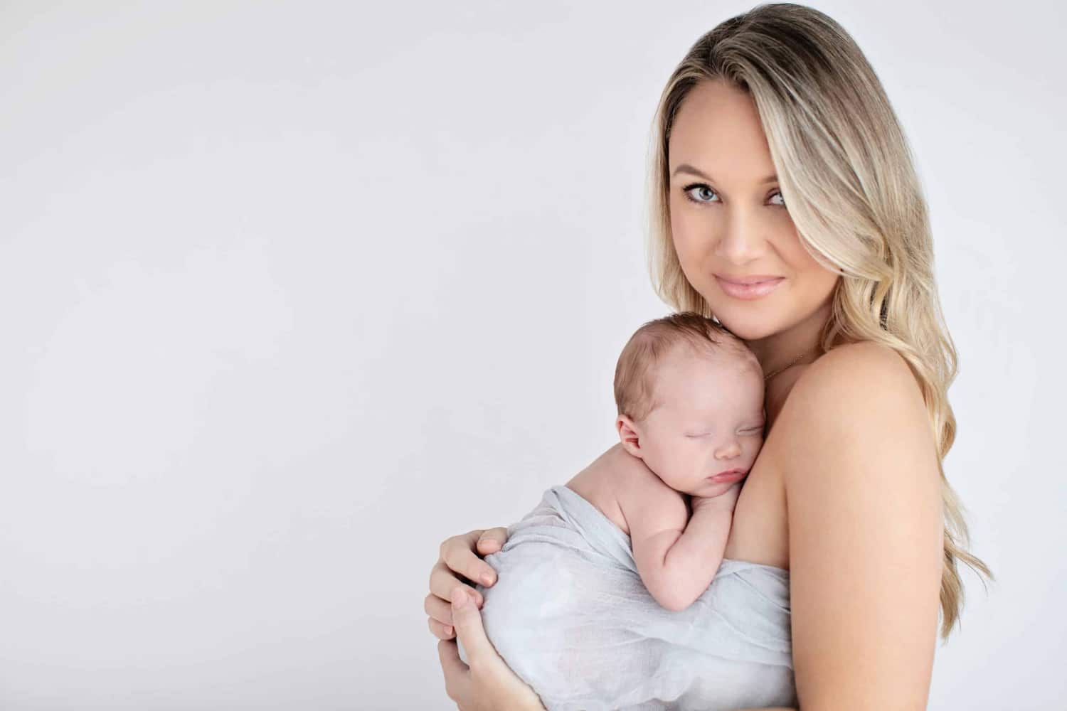 A woman holds her newborn baby in a gray wrap.