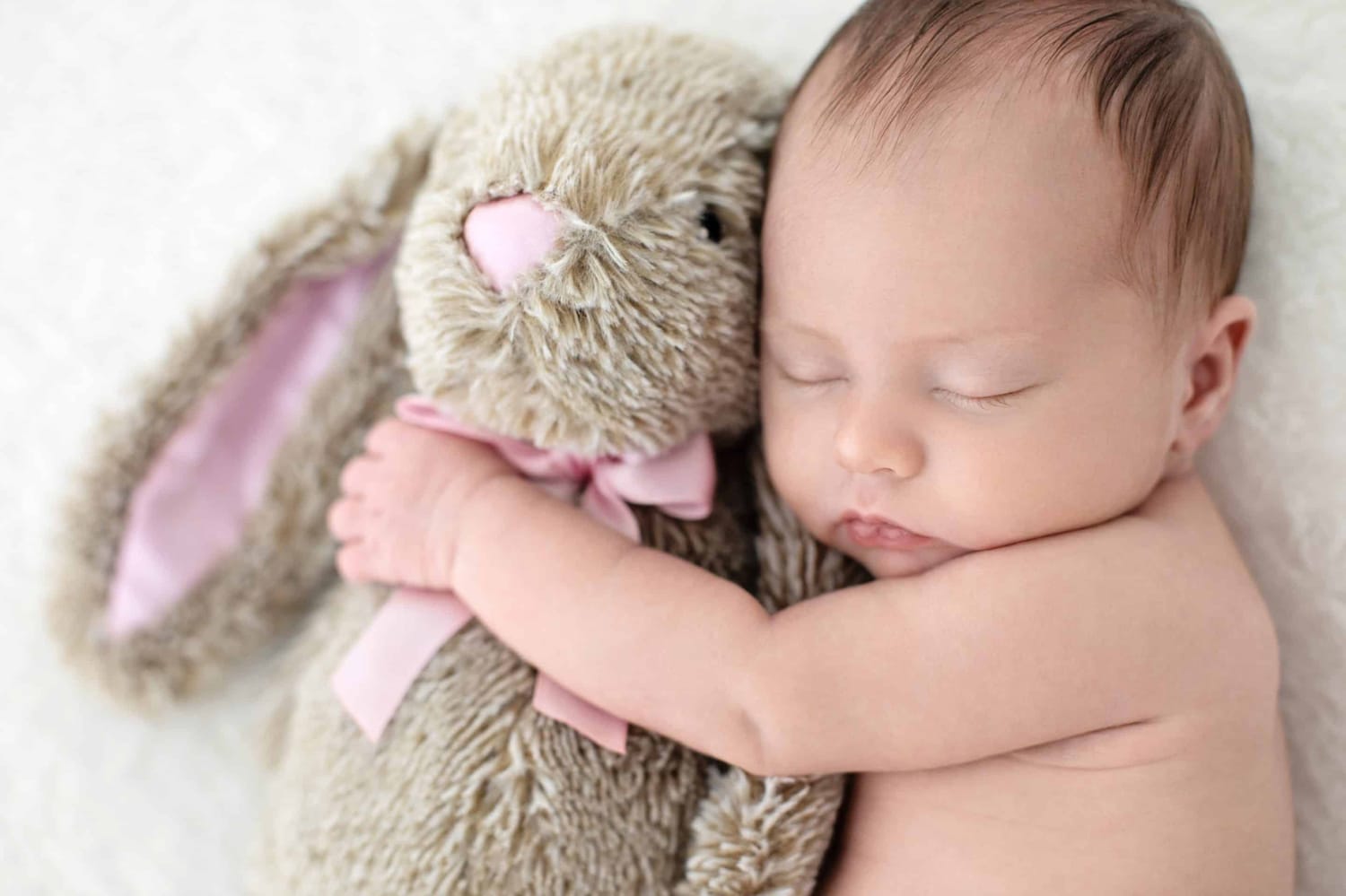 A newborn baby holds a stuffed rabbit.