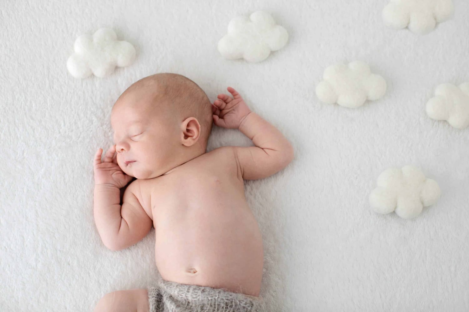 A baby lays under stuffed clouds.